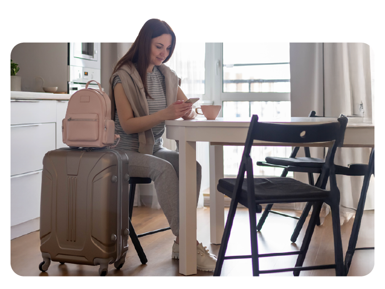 Usuária na cozinha de casa com malas, consultando o celular, preparada para viajar