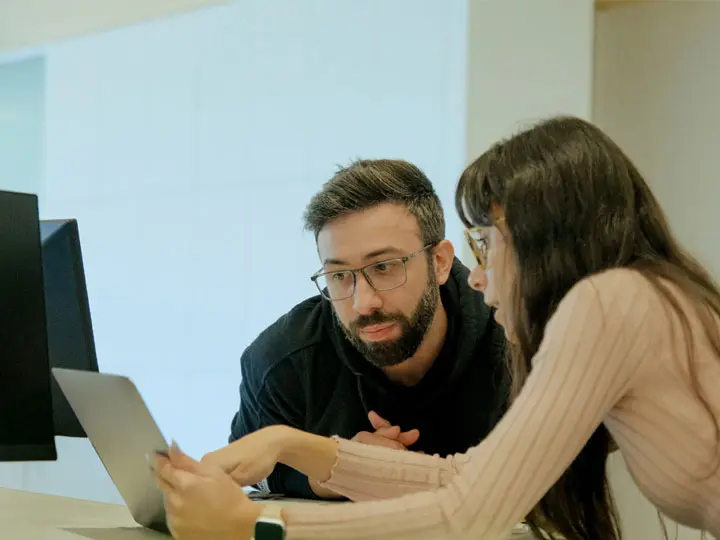 Dos miembros del equipo consultan algo en el portátil de uno de ellos