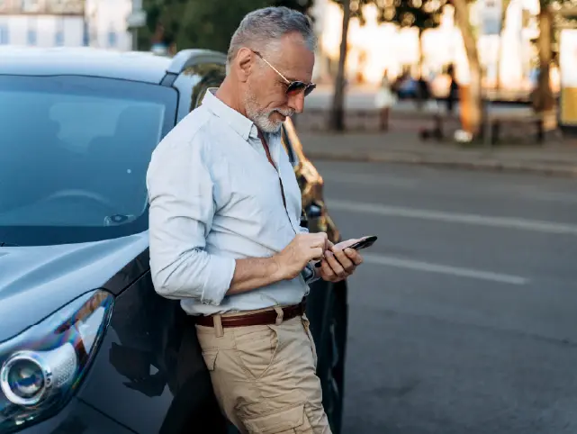 Usuario apoyado en un coche, consultando el móvil