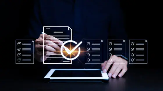 Una persona utiliza un lápiz digital con una tableta, sobre la que aparecen iconos digitales de documentos y marcas de verificación, representando la verificación o aprobación electrónica de documentos.